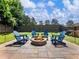Backyard stone firepit surrounded by blue Adirondack chairs on a paver patio with green grass at 5220 Southern Hills Ln, Cumming, GA 30040