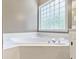 Close up of the bright bathroom featuring a large garden tub with tile surround and a privacy glass window at 25 Grange Ct, Sharpsburg, GA 30277