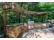 Outdoor kitchen with stone surround, stainless grill, and granite counters under pergola at 2101 Hunters Green Dr, Lawrenceville, GA 30043