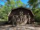 View of the barn with large doors, nestled among mature trees, adding extra outdoor storage at 5216 Wheeler Dr, Loganville, GA 30052