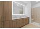 Modern bathroom with a large, illuminated mirror, double sinks, wood cabinets, and glass shower at 775 Juniper St # 212, Atlanta, GA 30308