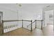 Second floor hallway boasts hardwood floors, neutral paint, with a view of the stairs and a modern chandelier beyond at 327 Awendaw Cir, Ellenwood, GA 30294