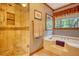 Well-lit bathroom featuring a shower and large soaking tub beneath a window with a wooded view at 2165 Robin Hood Trl, Cumming, GA 30040