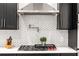 Close-up of kitchen with gas range, pot filler, white backsplash, stainless hood, and black cabinets at 132 Olympic Pl, Decatur, GA 30030