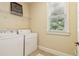 Bright laundry room with white washer and dryer, overhead shelving, and a window providing natural light at 5172 Roswell Rd, Marietta, GA 30062