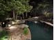 Night view of a sparkling backyard pool surrounded by mature trees and landscape lighting at 4601 Tall Pines Nw Dr, Atlanta, GA 30327
