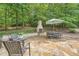 Outdoor stone patio featuring a fireplace, dining set, and umbrella in a lush, wooded backyard at 5940 Plantation Dr, Roswell, GA 30075
