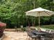 Stone patio with dining table and striped umbrella, surrounded by lush greenery, creating a relaxing outdoor space at 5940 Plantation Dr, Roswell, GA 30075