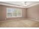 Carpeted bedroom featuring a tray ceiling, ceiling fan, and bright natural light from large window at 1684 Tailmore Ln, Lawrenceville, GA 30043