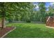 A well-maintained backyard with green grass, mature trees, wood fence, stone fire pit, and a wooden deck at 6890 Autumn Hills Dr, Cumming, GA 30028