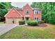 Charming two-story red brick home featuring a well-manicured lawn, attached two-car garage, and lush landscaping at 5765 Woodstone Dr, Cumming, GA 30028