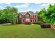 Charming two-story red brick home with a lush green lawn, complemented by mature trees and manicured landscaping at 209 Breckenridge Ct, Canton, GA 30115