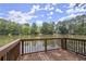 Wooden deck with a railing overlooking a serene lake surrounded by lush trees and blue skies at 3260 Kingshouse Commons, Johns Creek, GA 30022