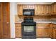 Wood cabinetry and black appliances in a kitchen with tile floors and stone backsplash at 5310 Arrowind Nw Rd, Lilburn, GA 30047