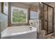 A garden tub sits next to a tiled shower with a glass enclosure, with a view from the window at 4305 Hunters Walk Way, Cumming, GA 30028