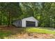 Detached white garage with a black door surrounded by lush green trees at 2871 Tucker Mill Sw Rd, Conyers, GA 30094