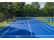 View of a blue and green community tennis court with net surrounded by trees and fencing at 6004 Turfway Park Ct, Sugar Hill, GA 30518