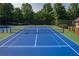 View of a well-maintained blue and green community tennis court surrounded by mature trees and fencing at 6004 Turfway Park Ct, Sugar Hill, GA 30518