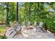 Stone fire pit encircled by gray Adirondack chairs on a brick patio in a wooded backyard at 1860 Hill Chase, Alpharetta, GA 30022