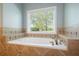 Close-up of a soaking tub with tile surround and a large window with blinds at 815 Spring View Ct, Covington, GA 30014