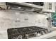 Close-up of gas cooktop with modern range hood and tile backsplash at 1870 Marcia Overlook Dr, Cumming, GA 30041