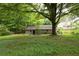 View of a large backyard with a small block building and a house in the background surrounded by trees at 1395 Clay Sw Rd, Mableton, GA 30126
