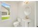 All-white half bath with pedestal sink, gold fixtures, and exterior view from window at 3932 E Saddle Ridge Dr, Lithonia, GA 30038