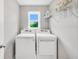 Bright laundry room with a side-by-side washer and dryer, storage shelf, and window view to the outside at 715 Colvin Dr, Locust Grove, GA 30248