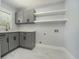Modern laundry room featuring gray cabinetry, floating shelves, and a convenient sink area with marble floors at 3470 Glenwood Rd, Decatur, GA 30032