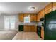 Clean kitchen featuring tan tiled floors, wood cabinets, black appliances, and access to a carpeted living area at 3694 Rolling Pl, Conley, GA 30288