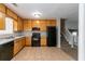 Functional kitchen with tan tiled floors, wood cabinets, a black appliance suite, and a view of the carpeted stairs at 3694 Rolling Pl, Conley, GA 30288