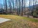 A sloped backyard with scattered trees, a partial view of a patio, and houses visible through the trees at 5728 Williams Rd, Norcross, GA 30093