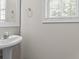 Elegant half-bathroom featuring a pedestal sink, decorative mirror, and natural light from the window at 3234 Baymount Way, Lawrenceville, GA 30043
