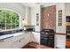 Charming kitchen features white cabinets, black countertops, farmhouse sink, brick wall, and an oversized window at 27 Sessions Nw St, Marietta, GA 30060
