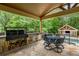 Covered outdoor kitchen with stone accents, a built-in grill, and a dining area overlooking the landscaped backyard at 816 Blackfoot Trl, Suwanee, GA 30024