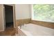 Bathroom showcasing a soaking tub with tile surround, a large window, and a doorway to a walk-in closet at 942 Idlewood Dr, Canton, GA 30115