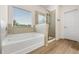 Well-lit bathroom features a tub under a window, a separate shower and wood-look floors, offering a serene atmosphere at 228 Whitneys Way, Dallas, GA 30157