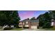 Dusk shot of a brick home with glowing windows, mature trees, and a long driveway, creating a warm ambiance at 285 Finsbury Park Ct, Suwanee, GA 30024