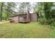 View of the home's rear exterior, featuring a small wooden deck and grassy backyard, surrounded by trees at 9383 Woodknoll Way, Jonesboro, GA 30238