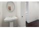 A stylish powder room with a pedestal sink, oval mirror, and dark wood flooring, adjacent to another room at 3330 Carswell Bnd, Cumming, GA 30028