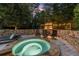 Outdoor hot tub featuring a stone surround, chairs, and a cozy fireplace under string lights at 979 Pathview Ct, Dacula, GA 30019