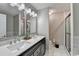 Bright bathroom features double sinks, a quartz countertop, stylish mirrors, and a tiled shower with a glass door at 1203 Penhurst Way, Lawrenceville, GA 30043