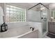 A full bathroom with a soaking tub, walk-in shower with glass enclosure, white tile, and a glass block window that provides natural lighting at 1143 Brookhaven North Cir, Brookhaven, GA 30319