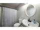 Bathroom featuring a shower-tub, gray shower curtain, white toilet, and sink with a round, white-framed mirror at 180 Mountain Path, Rockmart, GA 30153