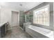 Bathroom boasts a garden tub beneath a custom window, a glass shower, and gray-tiled floors and walls at 5828 Paliser Trce, Sugar Hill, GA 30518