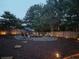 Backyard with a fire pit area surrounded by mulch and trees, illuminated by landscape lighting at 5445 Whisper Ct, Cumming, GA 30028