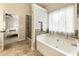 Bright bathroom featuring a large soaking tub, glass shower, tile flooring, and view into the main bedroom at 1650 Walking Horse Trl, Cumming, GA 30041