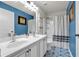 Well-lit bathroom with double sink vanity, patterned floor, blue accent wall, and shower with curtain at 2239 Noelle Pl, Powder Springs, GA 30127