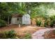 Backyard storage shed with double doors, situated amongst mature landscaping and a stone path at 1100 Tuxedo Dr, Roswell, GA 30075