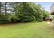 Grassy backyard with mature trees and shrubbery bordering a home with a wooden deck in the background at 1565 Briergate Dr, Duluth, GA 30097